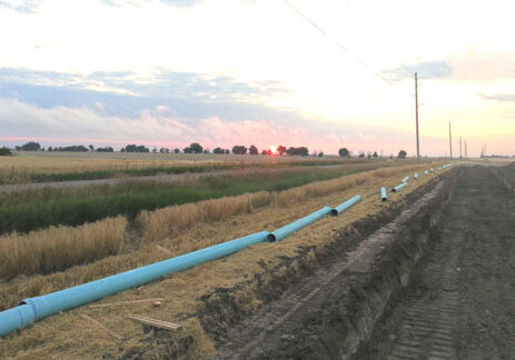 A blue pipe in the middle of a field at sunset.