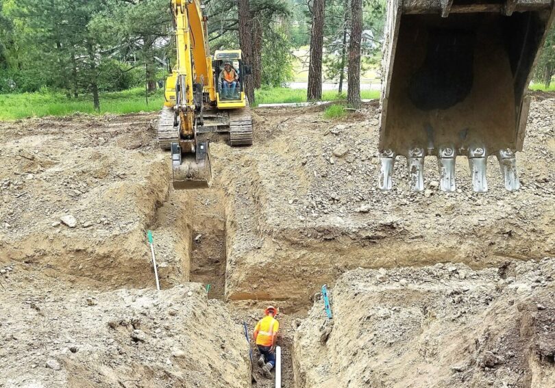 An excavator is digging a trench in a wooded area.